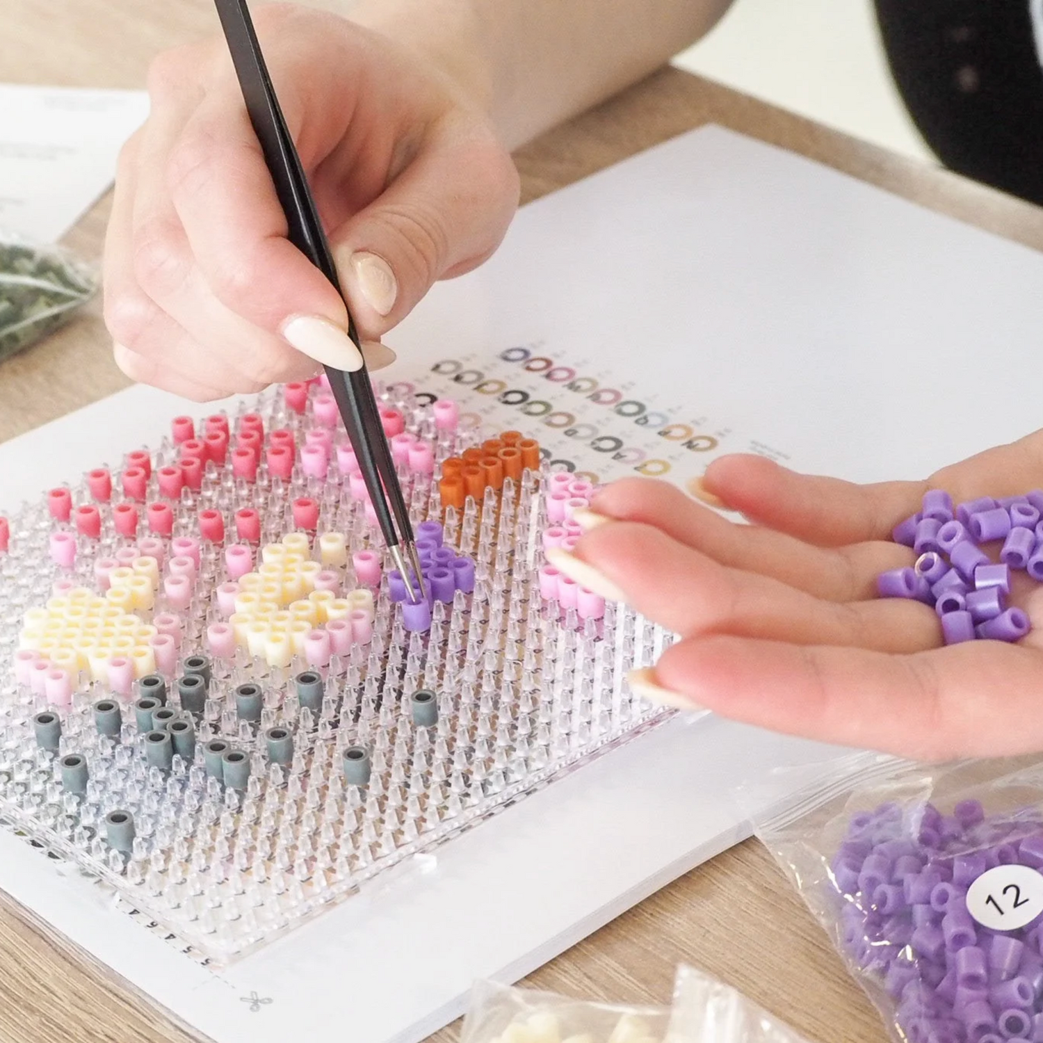 Kvinde hygger sig med kreativt hobby projekt med perleplade, perler og pincet